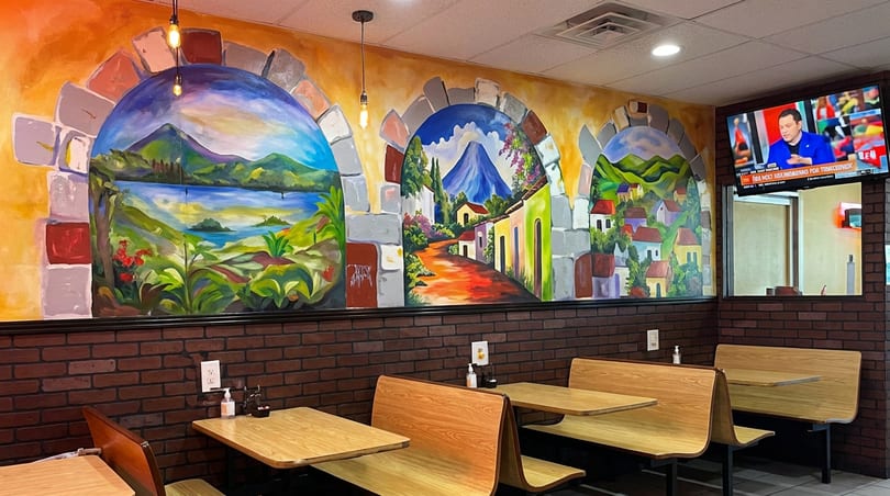 Colorful mural of landscapes and villages above wooden booths and tables in a restaurant.